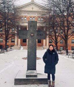 Kristy Hu stands in front of Bockman Hall on the Luther Seminary campus with snow-covered grouns
